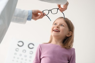 Vision testing. Ophthalmologist giving glasses to little girl indoors, low angle view