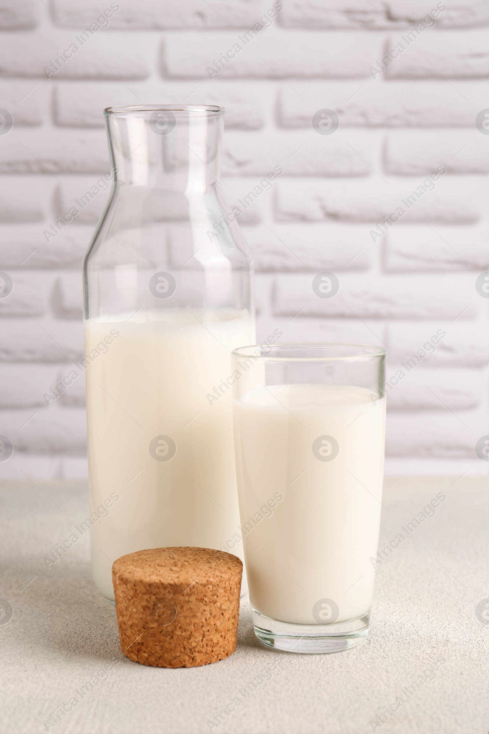 Photo of Glass and bottle of fresh milk on white table against brick wall