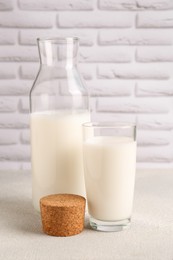 Glass and bottle of fresh milk on white table against brick wall