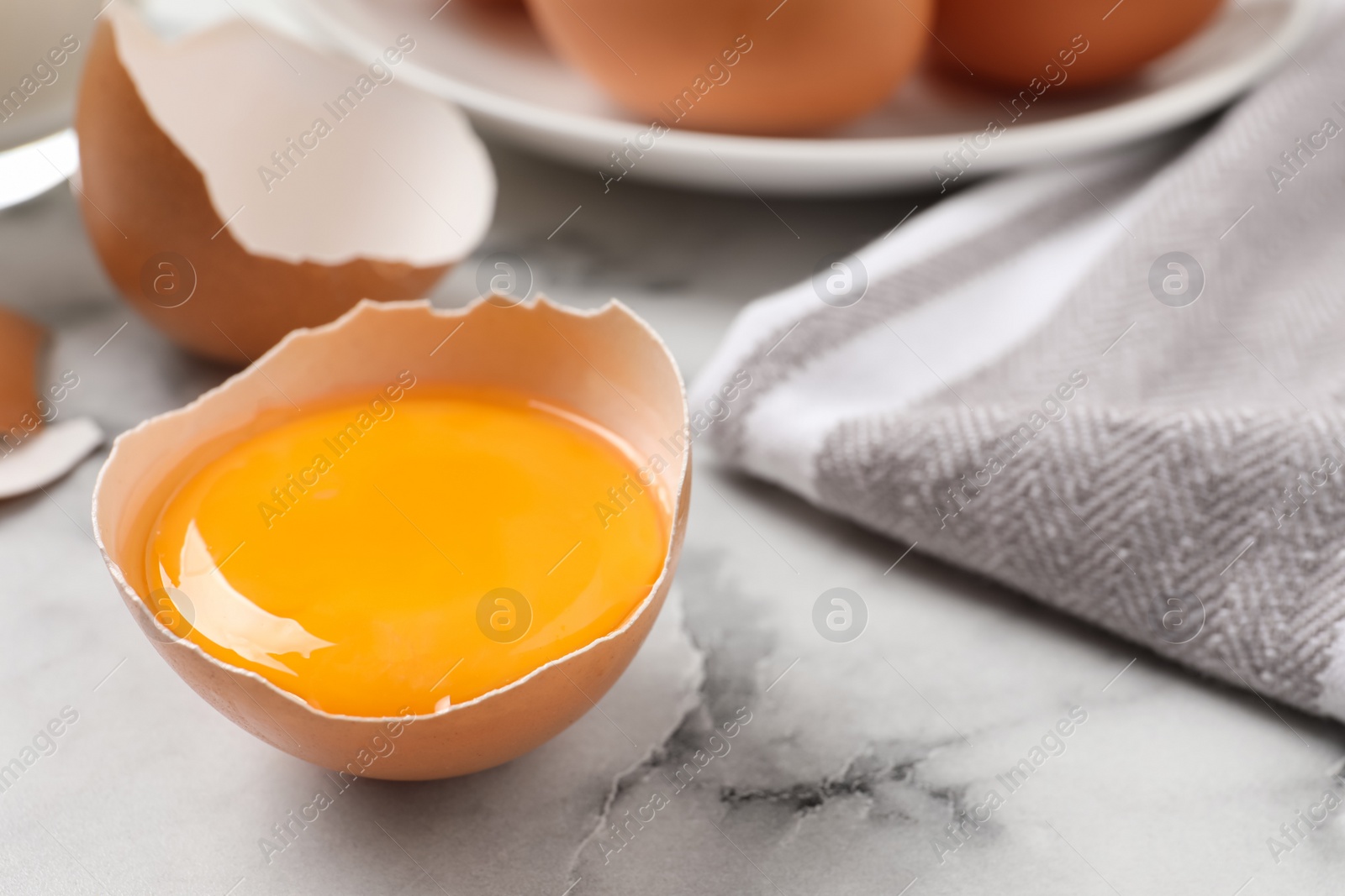 Photo of Cracked eggshell with raw yolk on white marble table, closeup. Space for text