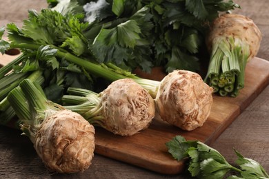 Photo of Fresh raw celery roots and leaves on wooden table, closeup