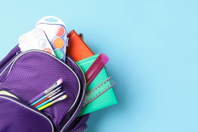 Photo of Stylish backpack with different school stationery on light blue background, top view and space for text. Back to school