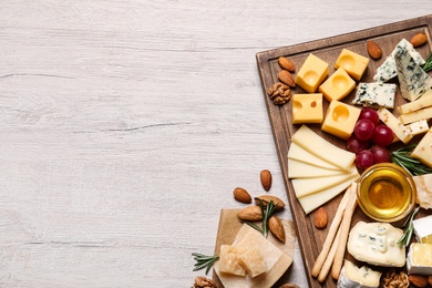 Photo of Cheese plate with honey, grapes and nuts on white table, flat lay. Space for text