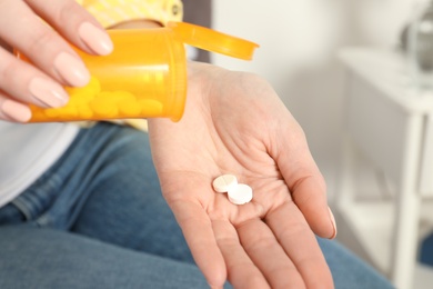 Woman pouring pills from bottle into hand indoors, closeup