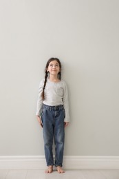 Photo of Little girl measuring her height near light grey wall indoors