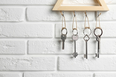 Photo of Wooden key holder on white brick wall indoors, closeup. Space for text