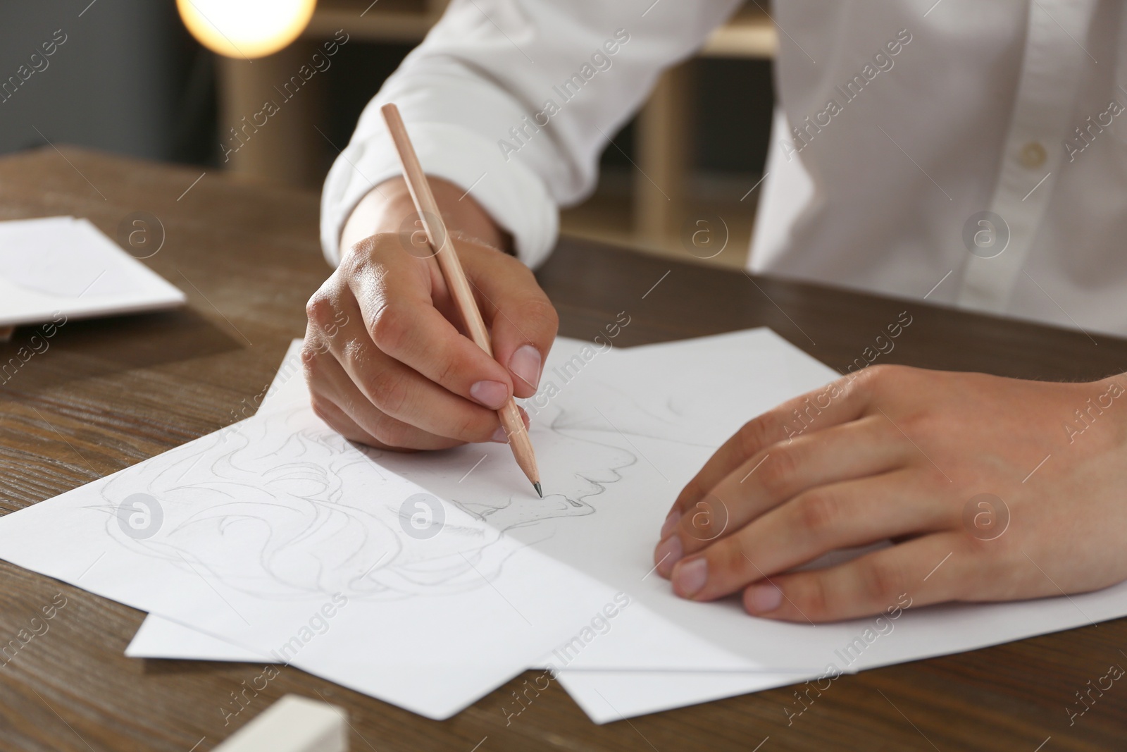 Photo of Man drawing portrait with pencil on sheet of paper at wooden table, closeup