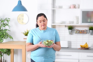 Photo of Overweight woman with bowl of salad in kitchen. Healthy diet