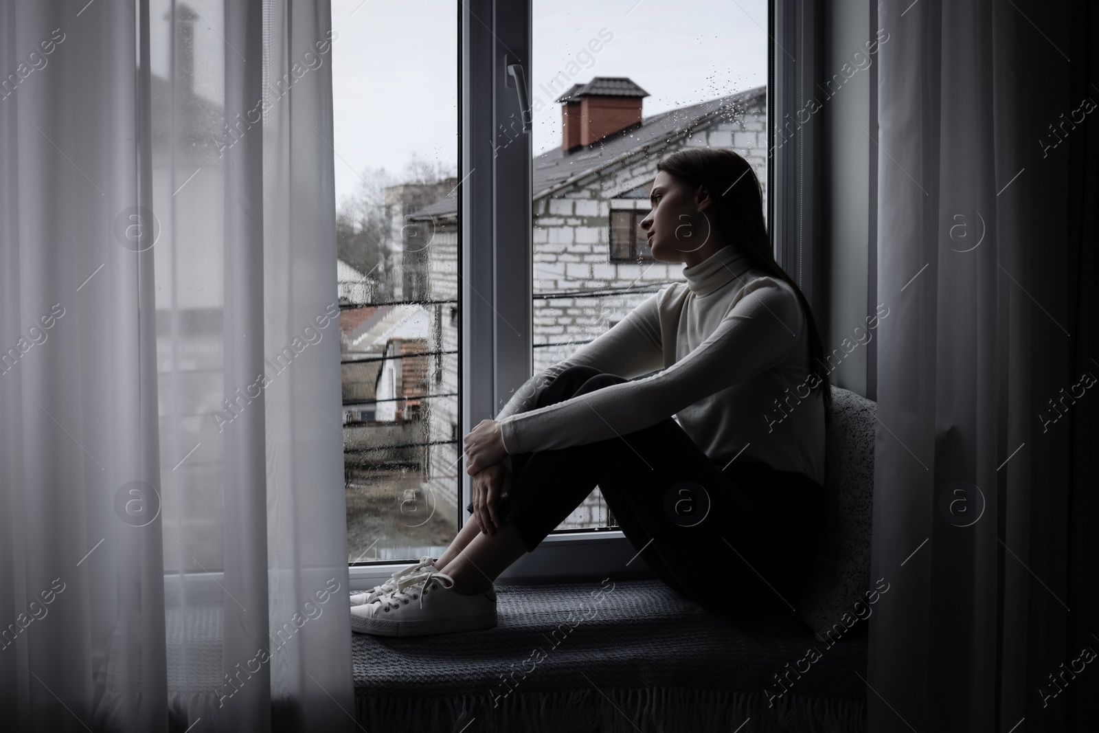 Photo of Melancholic young woman looking out of window indoors, space for text. Loneliness concept