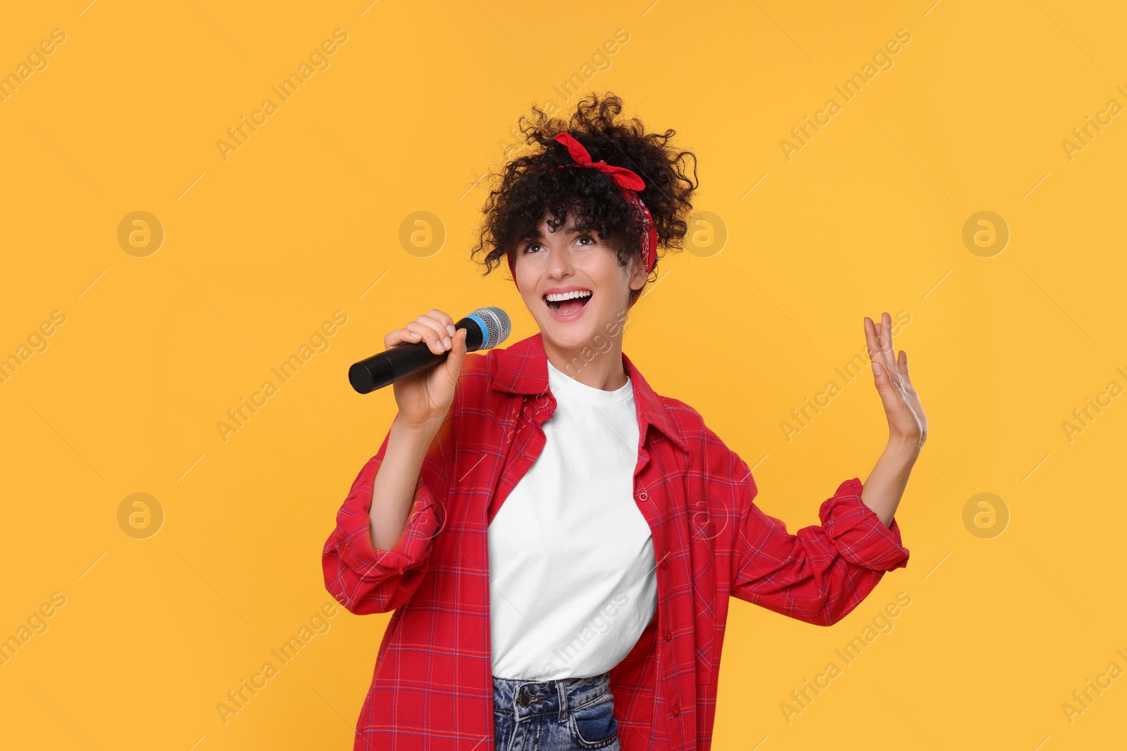 Photo of Beautiful young woman with microphone singing on yellow background