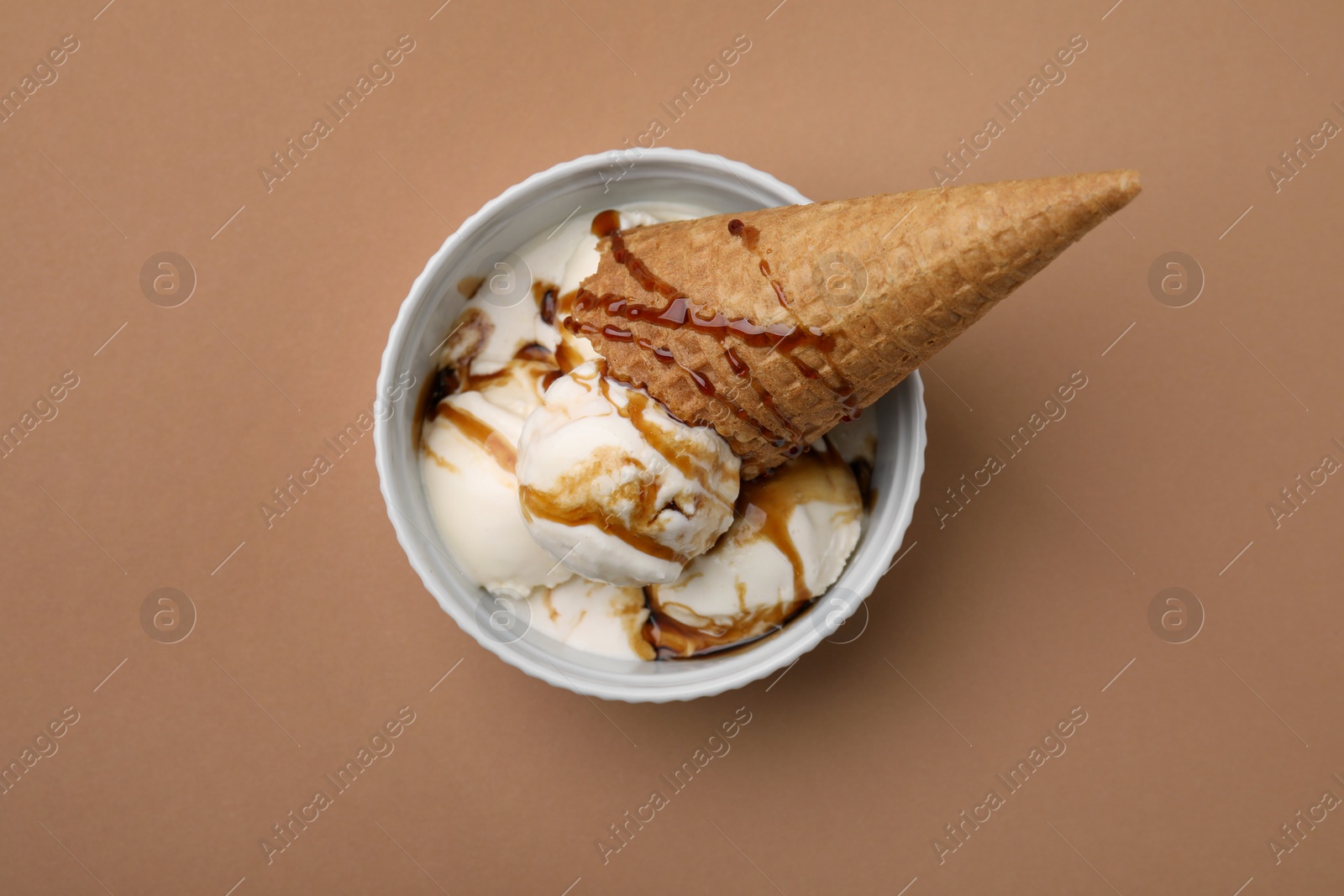 Photo of Scoops of ice cream with caramel sauce and wafer cone on light brown table, top view