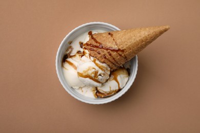 Photo of Scoopsice cream with caramel sauce and wafer cone on light brown table, top view