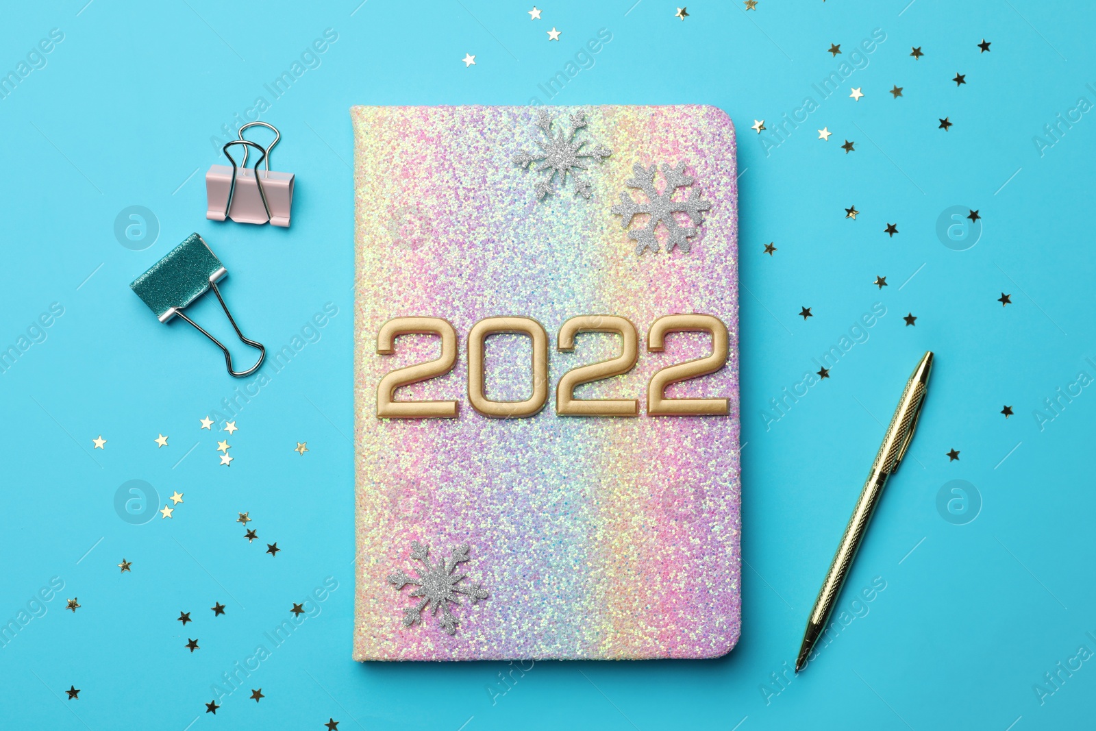 Photo of Bright planner, pen, stationery, decorative snowflakes and confetti on light blue background, flat lay. Planning for 2022 New Year