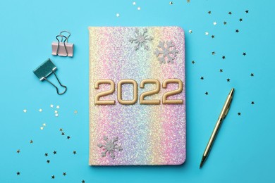 Photo of Bright planner, pen, stationery, decorative snowflakes and confetti on light blue background, flat lay. Planning for 2022 New Year