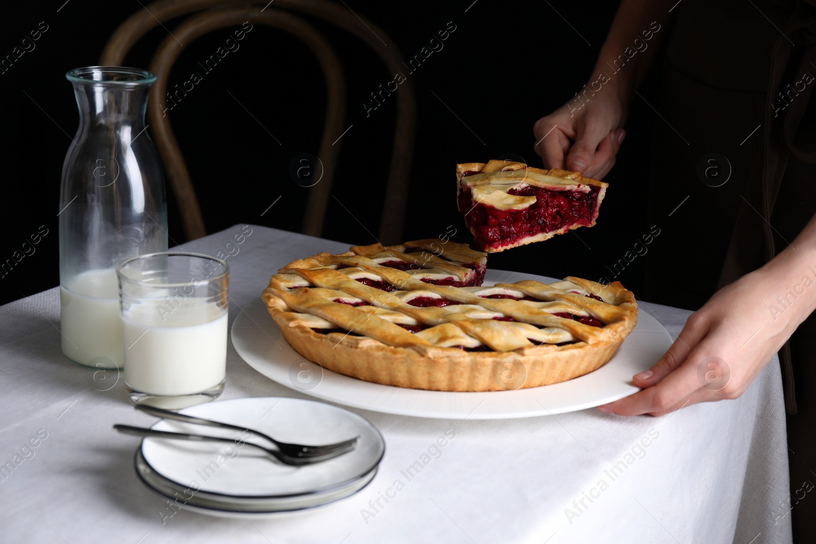 Photo of Woman taking slice of delicious cherry pie at table against dark background, closeup