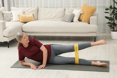 Senior woman doing exercise with fitness elastic band on mat at home