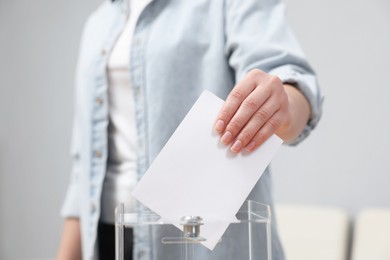 Photo of Woman putting her vote into ballot box on blurred background, closeup