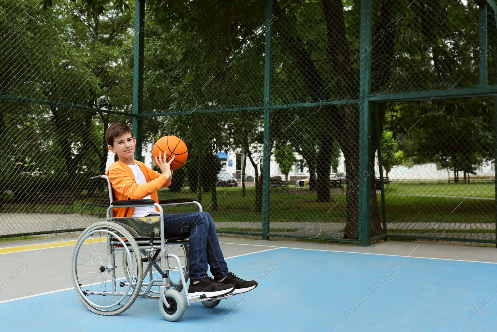 Photo of Disabled teenage boy in wheelchair playing basketball  on outdoor court