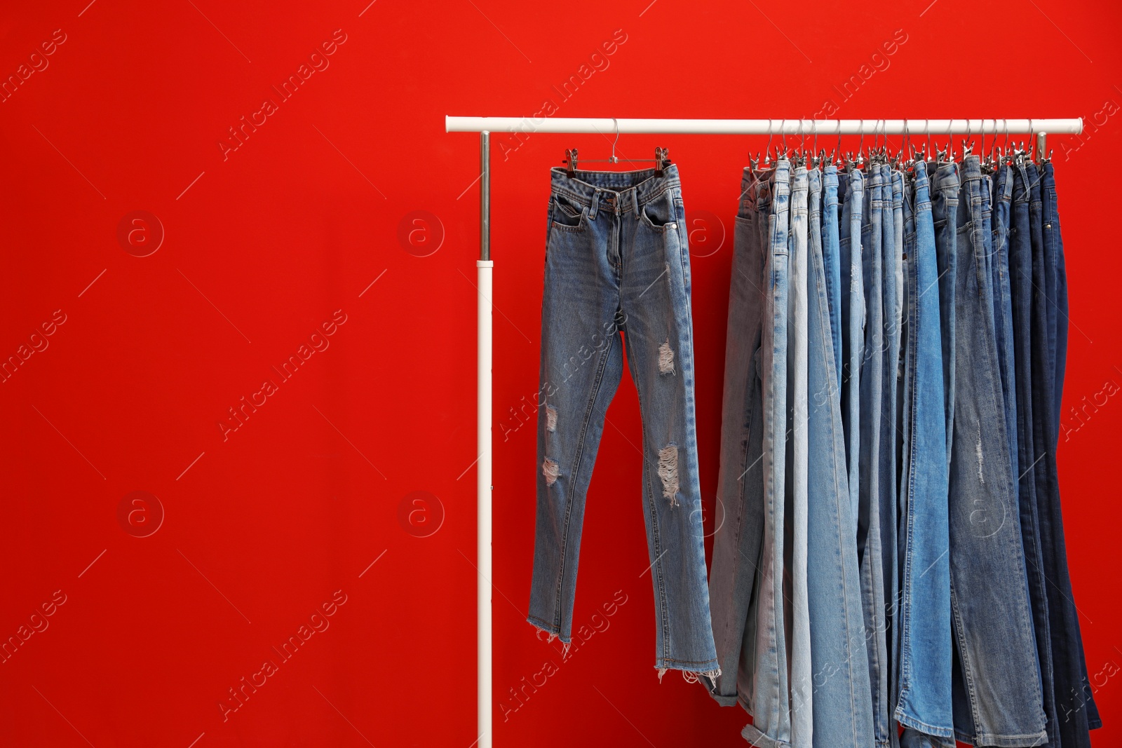 Photo of Rack with stylish jeans on red background. Space for text