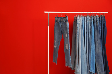 Photo of Rack with stylish jeans on red background. Space for text