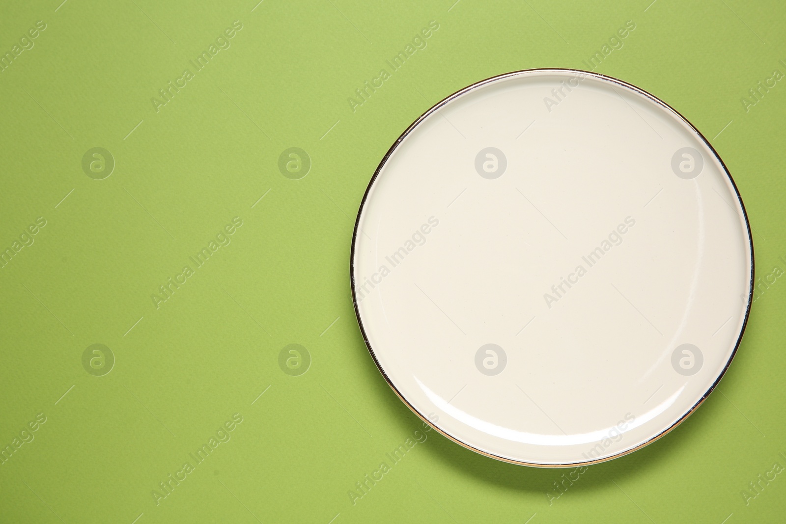 Photo of One white plate on green background, top view. Space for text