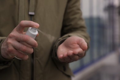 Photo of Man spraying antiseptic on his hand outdoors, closeup
