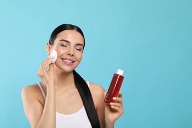 Photo of Young woman using cotton pad with micellar water on light blue background, space for text