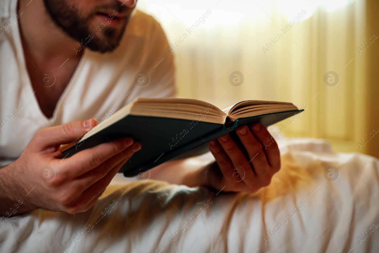 Photo of Young man reading book on bed at home, closeup