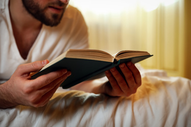 Young man reading book on bed at home, closeup