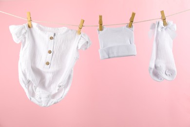 Baby clothes and accessories hanging on washing line against pink background