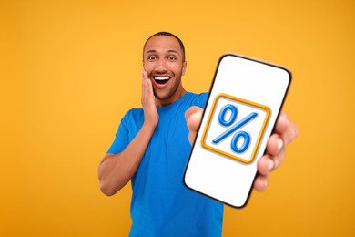 Image of Discount, offer, sale. Emotional man showing mobile phone with percent sign on screen, orange background