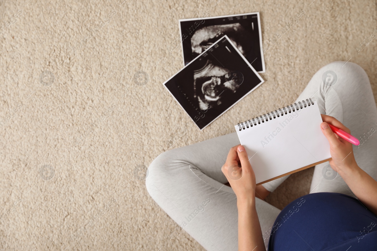 Photo of Pregnant woman with notebook and sonogram choosing name for baby on carpet, top view. Space for text