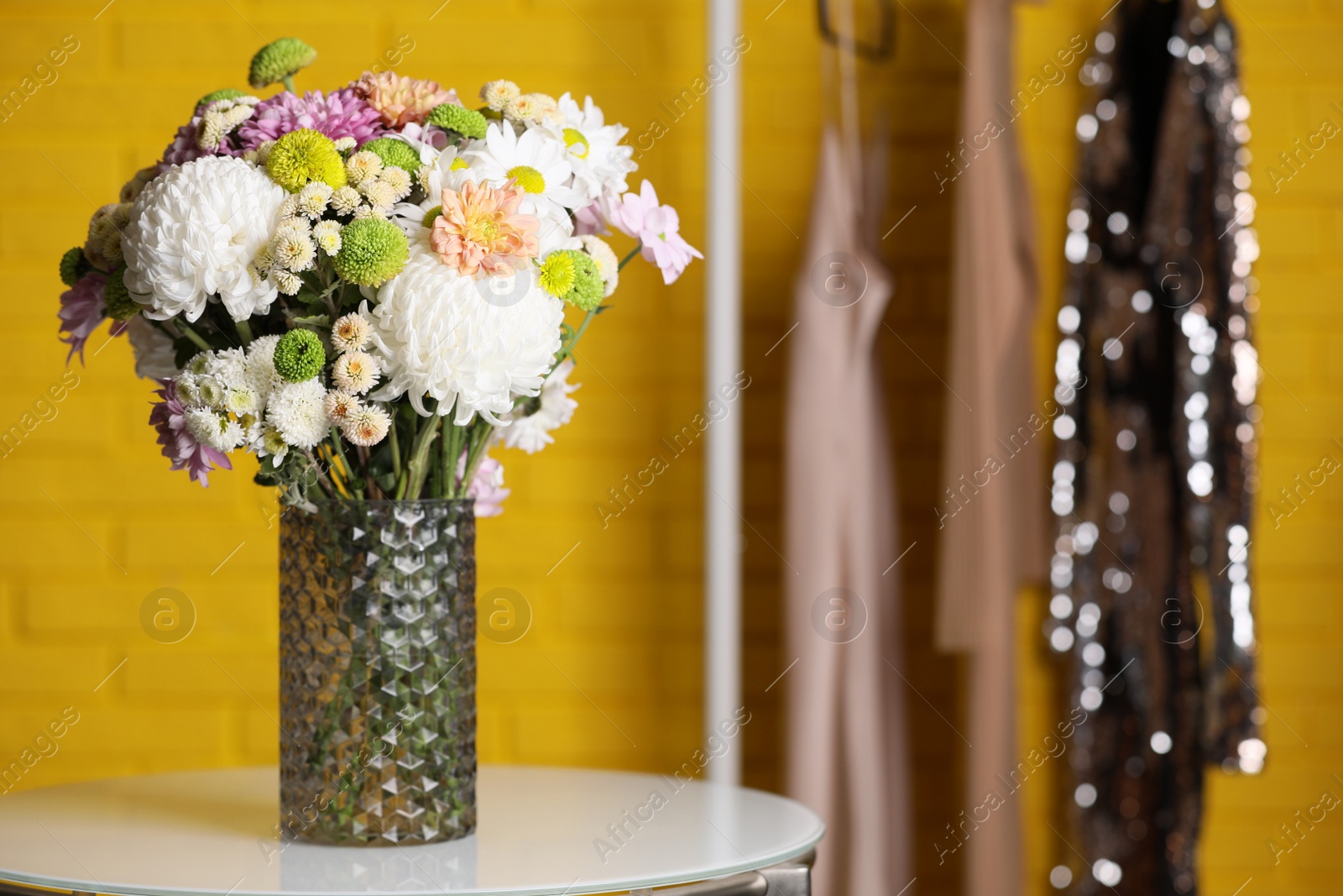 Photo of Bouquet of beautiful chrysanthemum flowers on white table against yellow brick wall, space for text