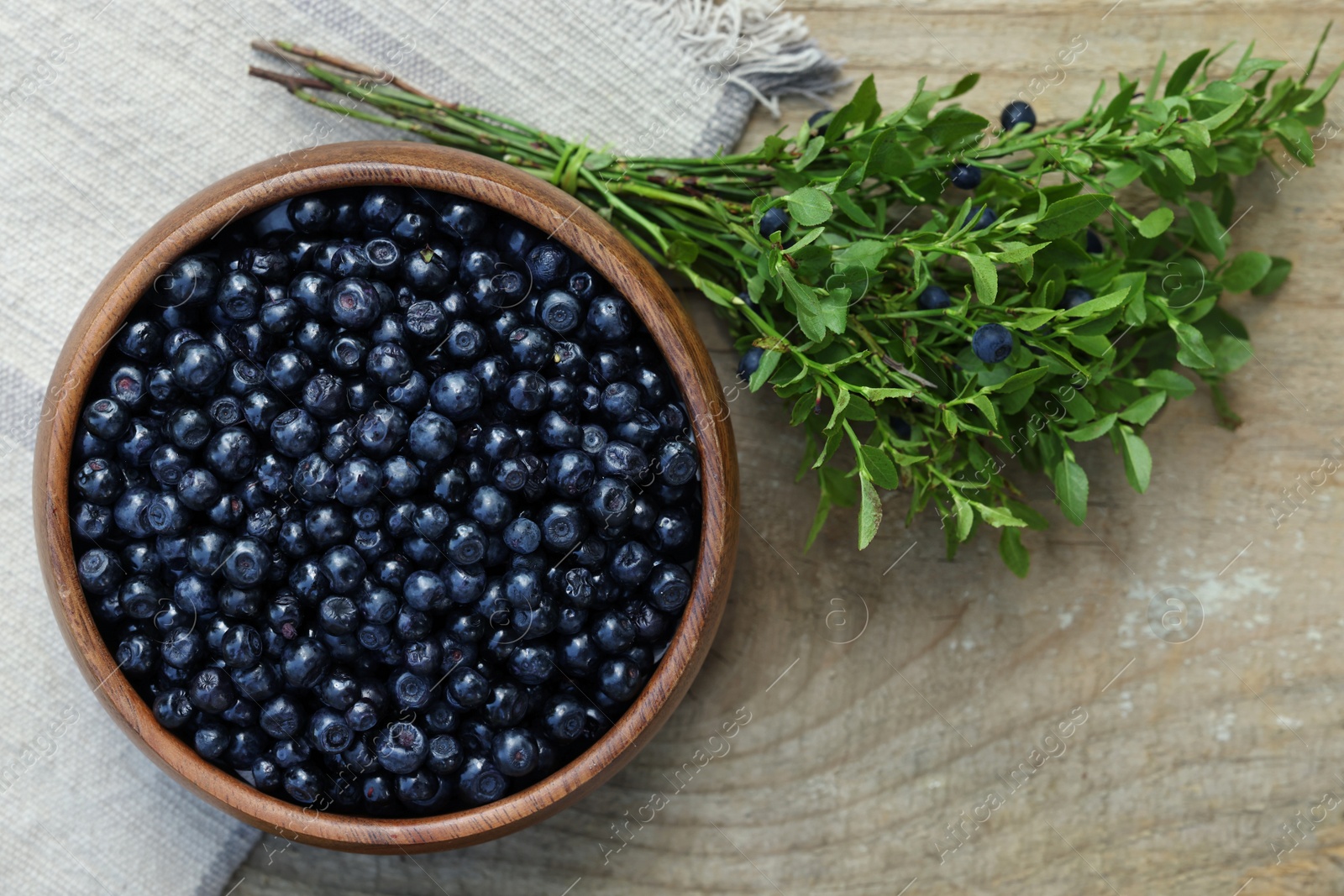 Photo of Delicious bilberries in bowl and branch with fresh berries on wooden table, flat lay