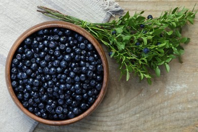 Photo of Delicious bilberries in bowl and branch with fresh berries on wooden table, flat lay