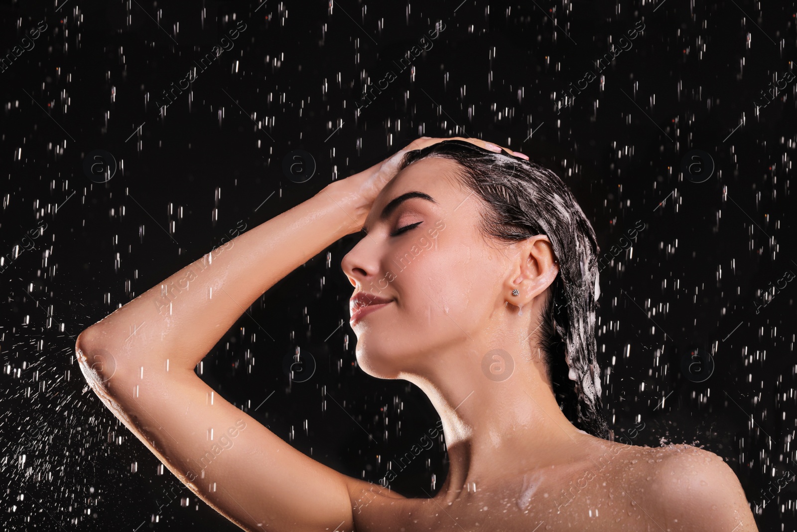 Photo of Young woman washing hair while taking shower on black background