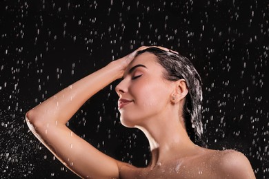 Photo of Young woman washing hair while taking shower on black background