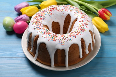 Glazed Easter cake with sprinkles, painted eggs and tulips on blue wooden table, closeup