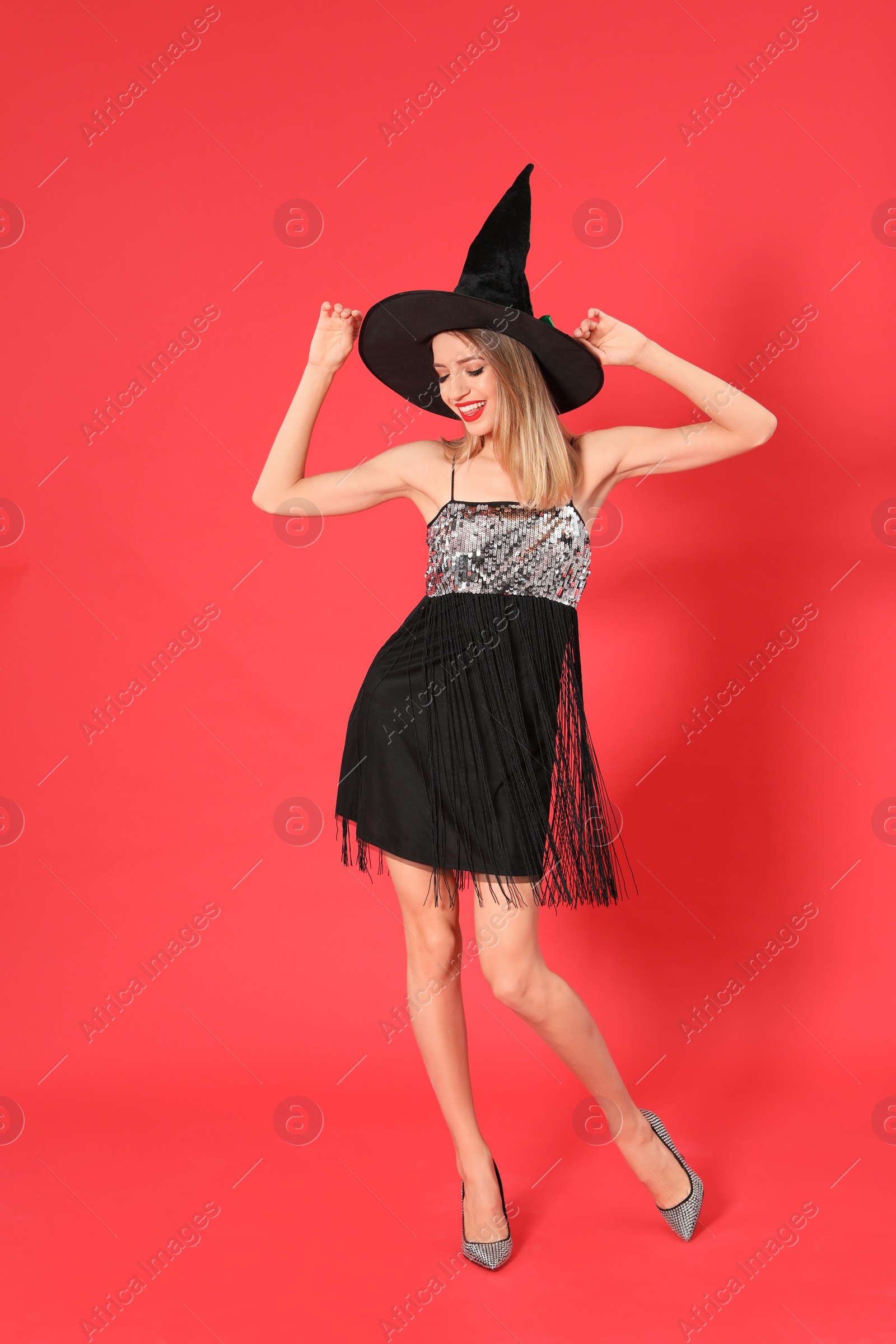 Photo of Beautiful young woman wearing witch costume for Halloween party on red background