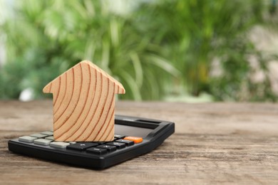 Mortgage concept. Model house and calculator on wooden table against blurred green background, space for text