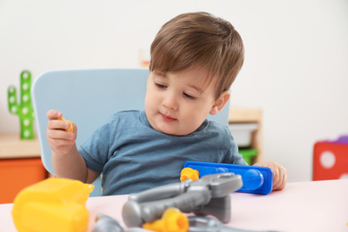 Little child playing with toy construction tools at table