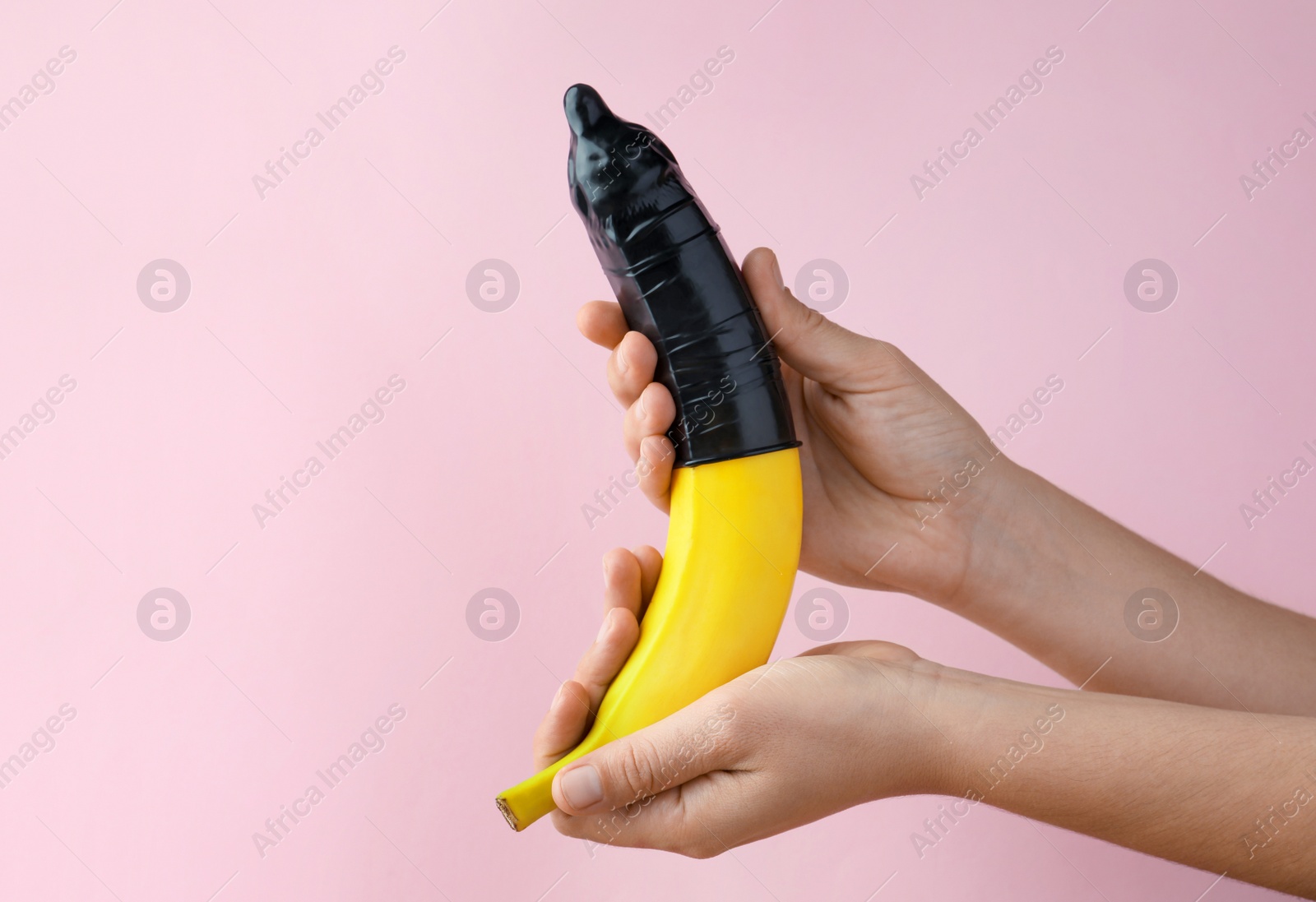 Photo of Woman holding banana in condom on pink background, closeup. Safe sex concept