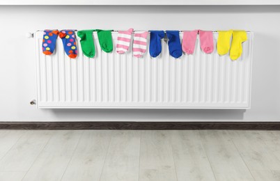 Different colorful socks on heating radiator near white wall