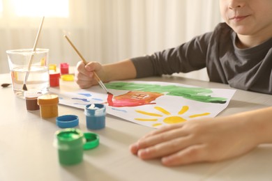 Little boy drawing picture with brush at wooden table indoors, closeup. Child`s art