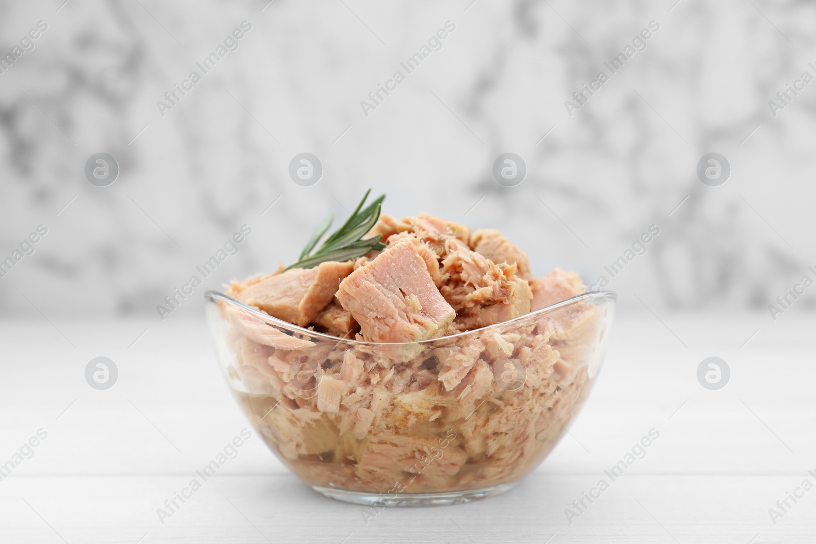 Photo of Bowl with canned tuna and rosemary on wooden table near white marble wall, closeup