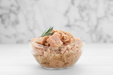 Photo of Bowl with canned tuna and rosemary on wooden table near white marble wall, closeup