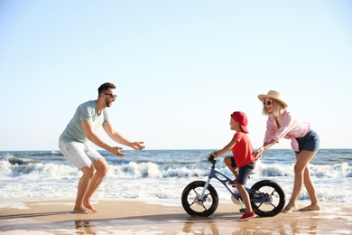 Photo of Happy parents teaching son to ride bicycle on sandy beach near sea