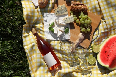 Picnic blanket with delicious food and wine on green grass outdoors, top view