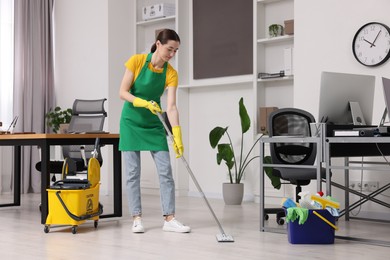 Cleaning service worker washing floor with mop. Bucket with supplies in office