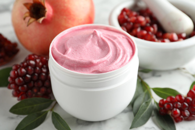 Fresh pomegranate and jar of facial mask on white marble table, closeup. Natural organic cosmetics